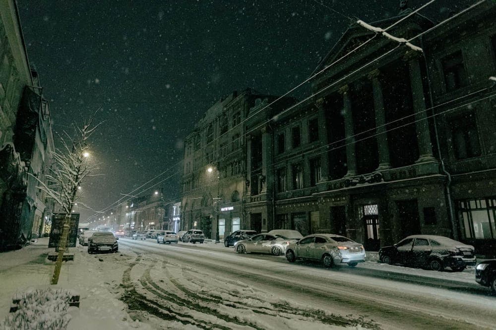 Snow falling on cars parked on a street at night