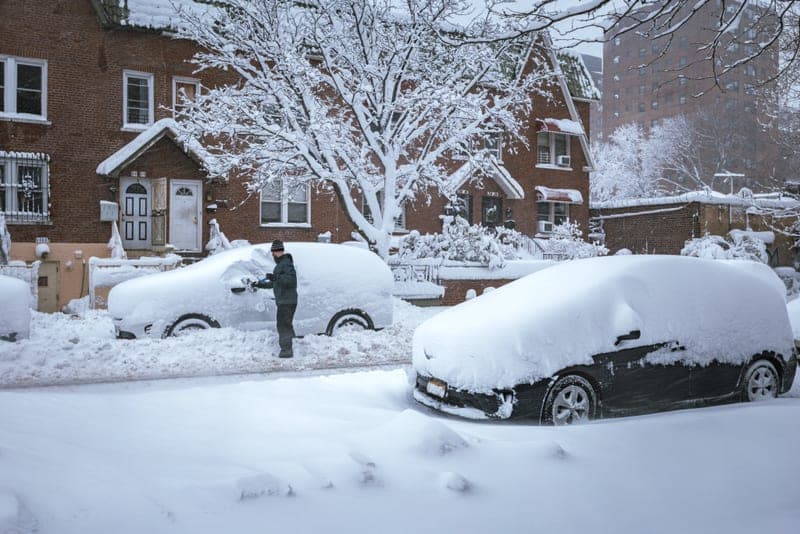 Snow being cleared from a car roof with a long-handled brush - a stand-in for the Snow Joe SJBLD 2-In-1 Telescoping Snow Broom and Ice Scraper, not a photograph of this model
